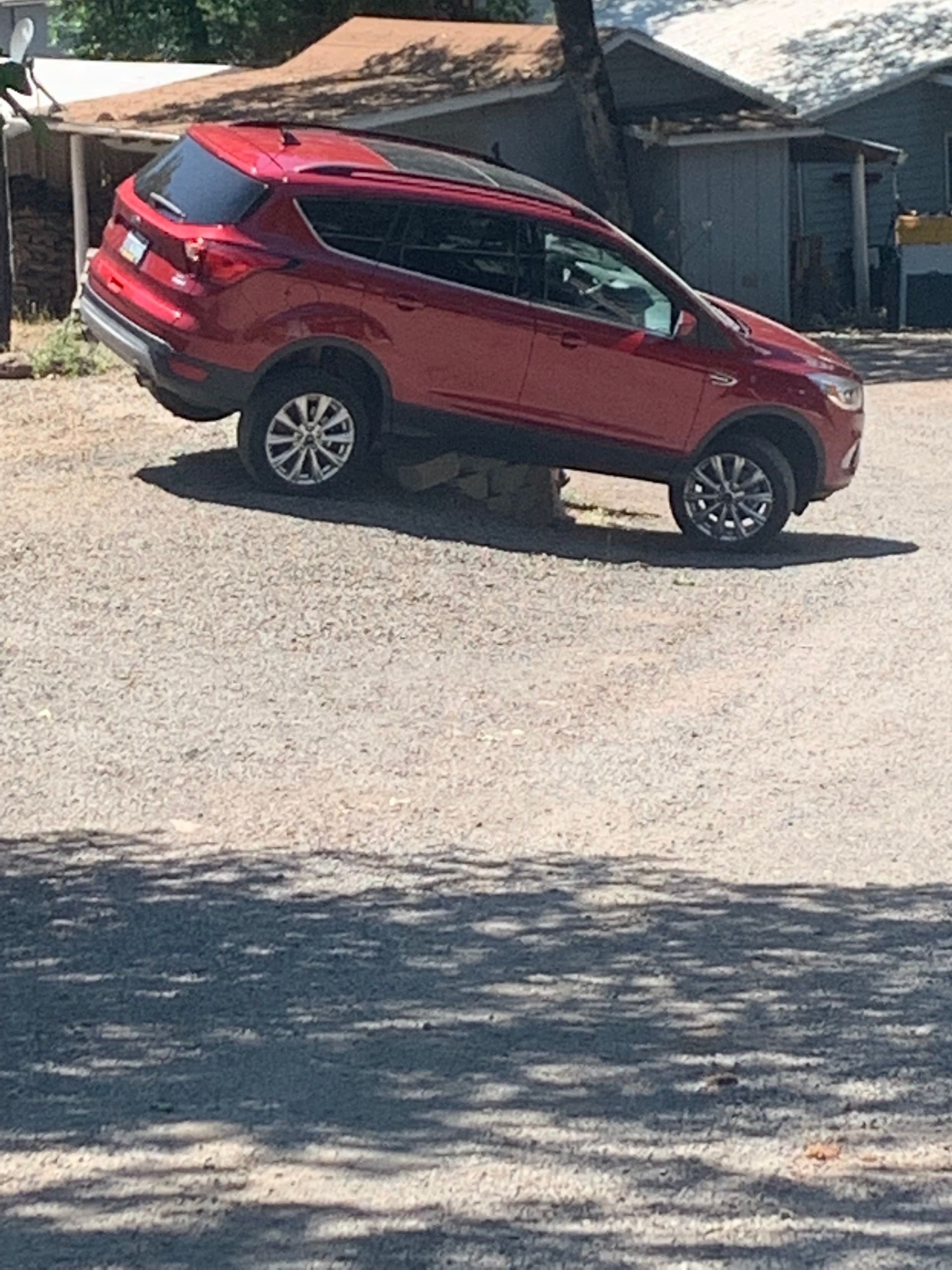 A red suv is parked in a gravel lot in front of a house.