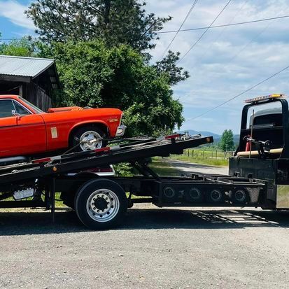 A red car is being towed by a tow truck.