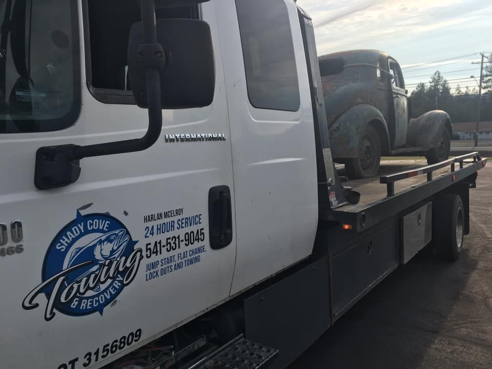 A towing truck with a car on the back is parked in a parking lot.