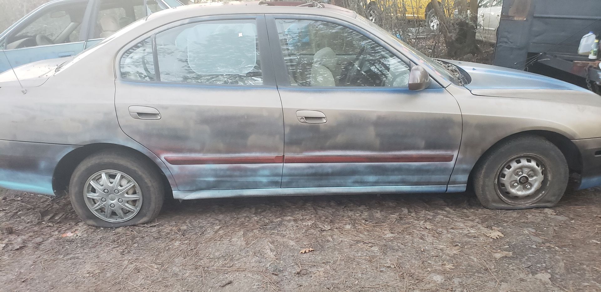 A car with a flat tire is parked in a gravel lot.