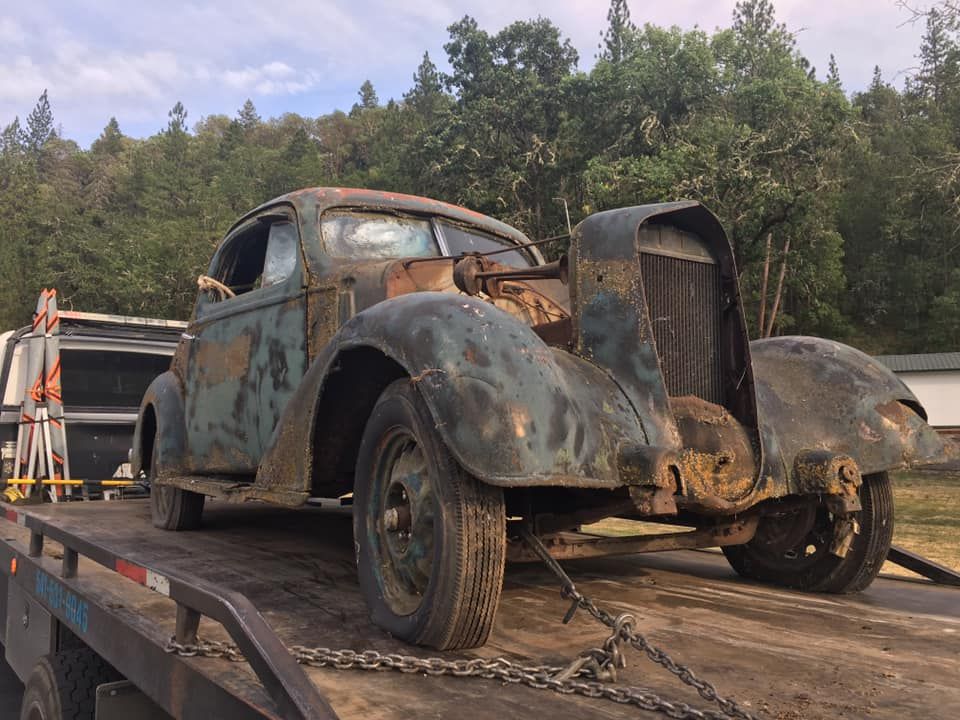 An old rusty car is sitting on top of a tow truck.