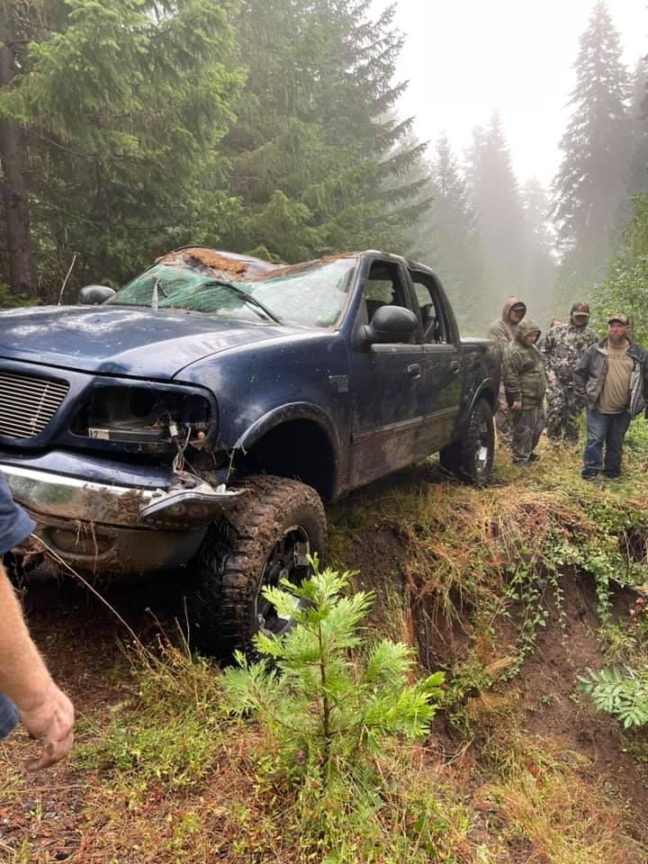 A truck is stuck in the mud on a dirt road in the woods.