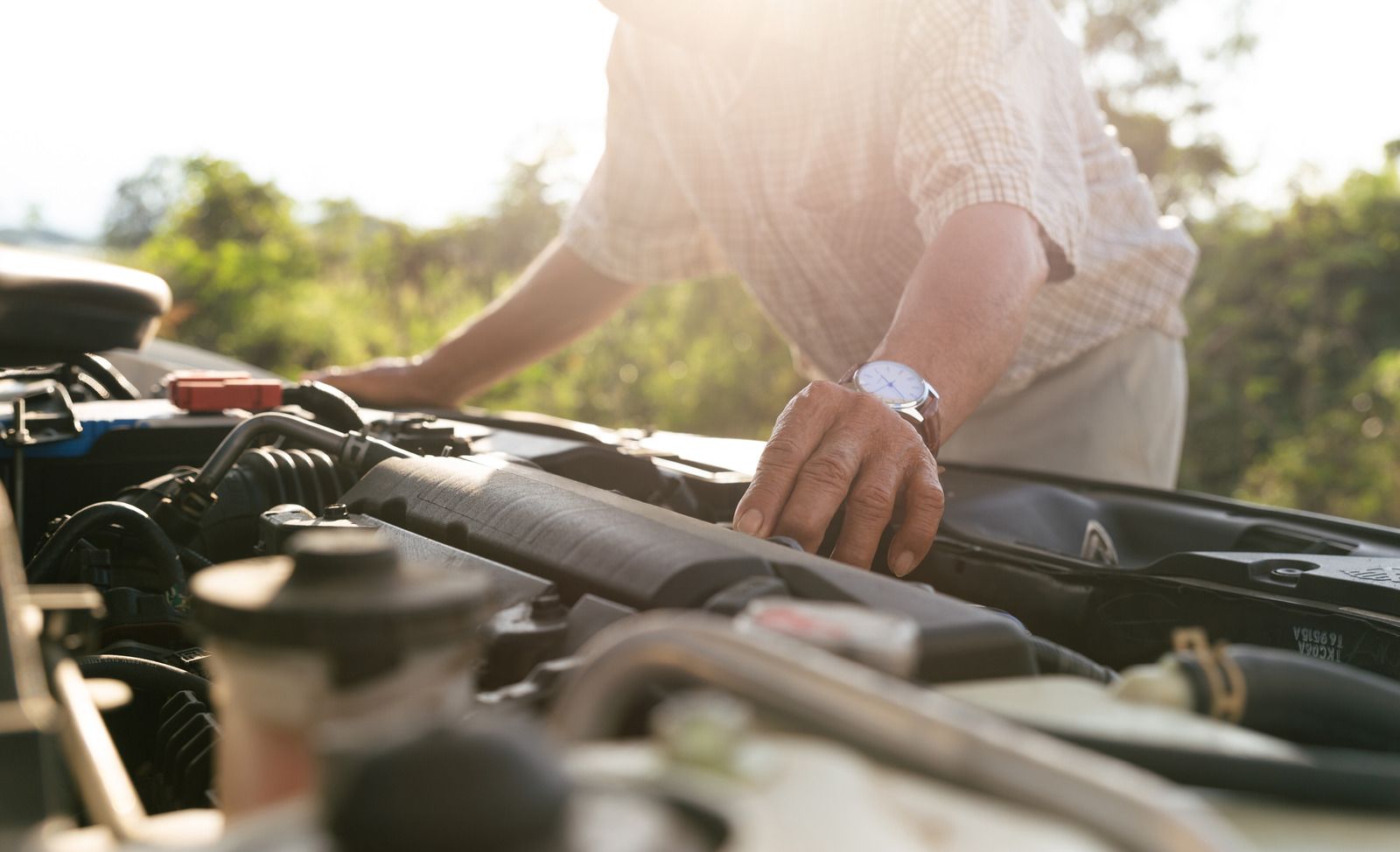 A man is looking under the hood of a car.