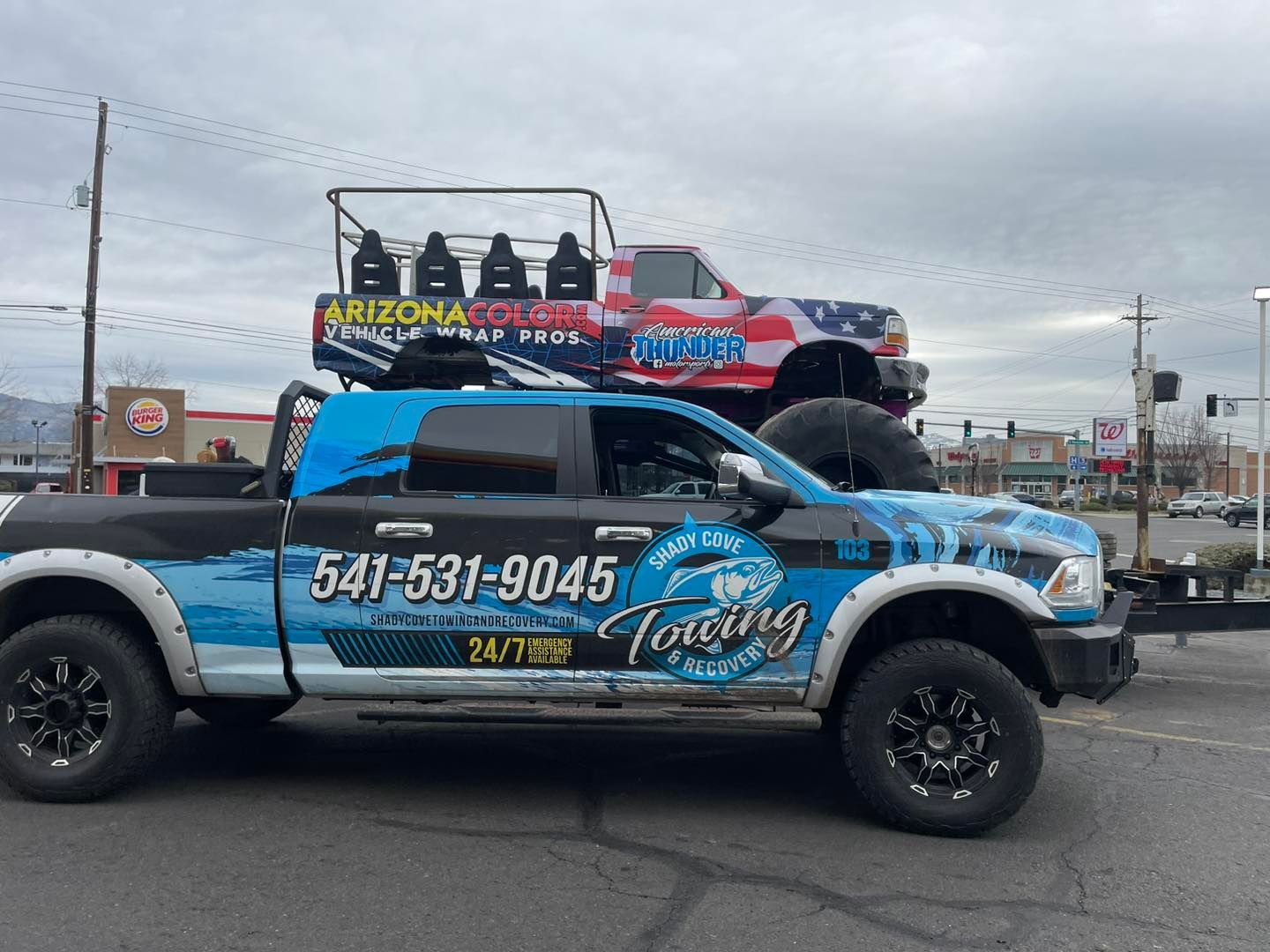 A truck with a jeep on top of it is parked on the side of the road.