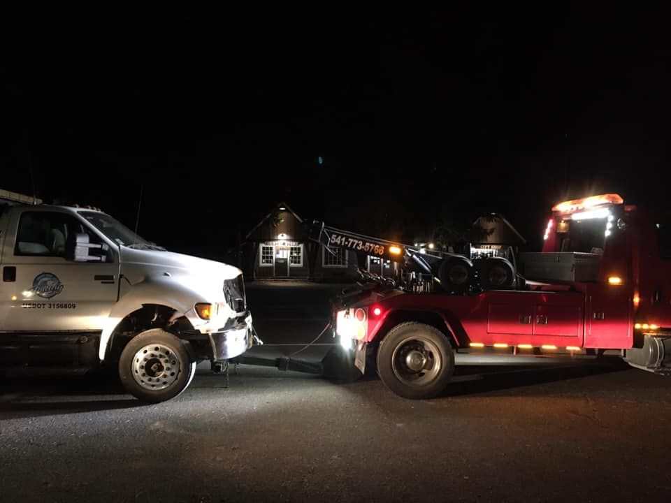 A red tow truck is towing a white truck at night.