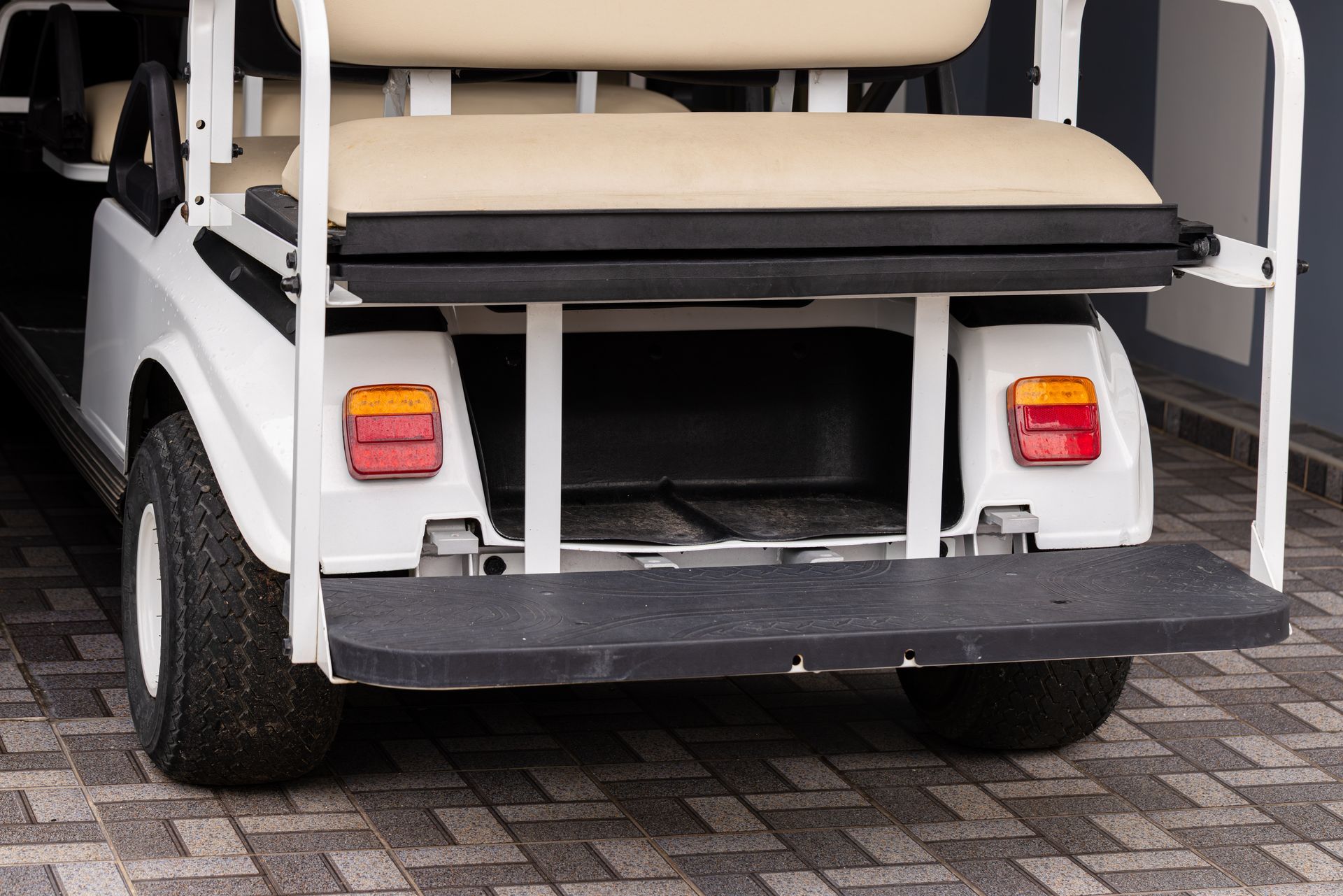 Rear view of a white golf cart with beige seats parked on a tiled pavement
