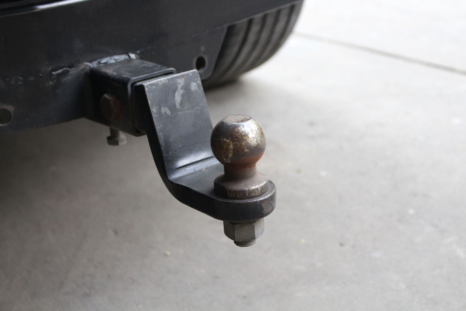Trailer hitch ball on a black vehicle, close-up on a concrete surface.