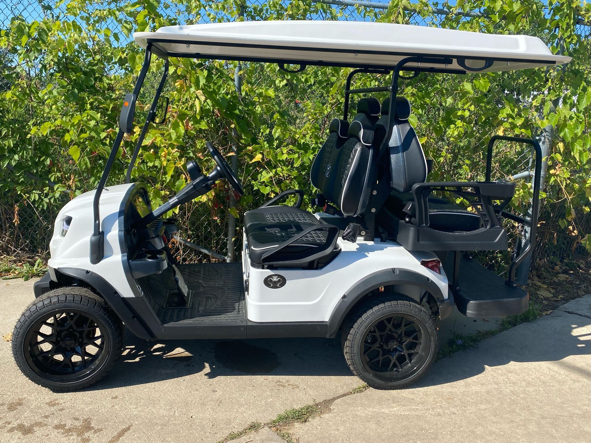 White golf cart parked on a road beside trees, with black seats and a canopy.