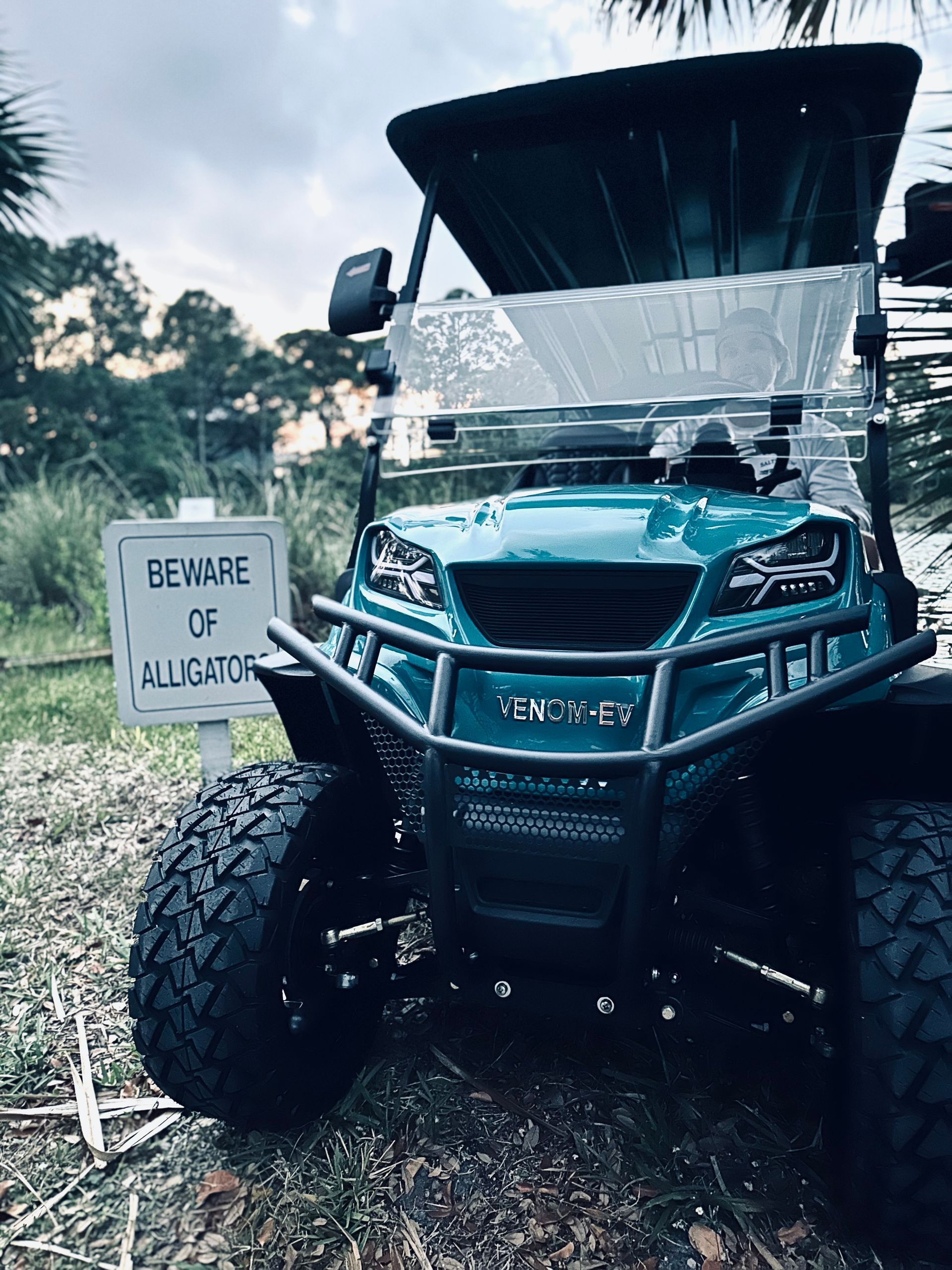 All-terrain vehicle beside a “Beware of Alligators” sign in a wooded area