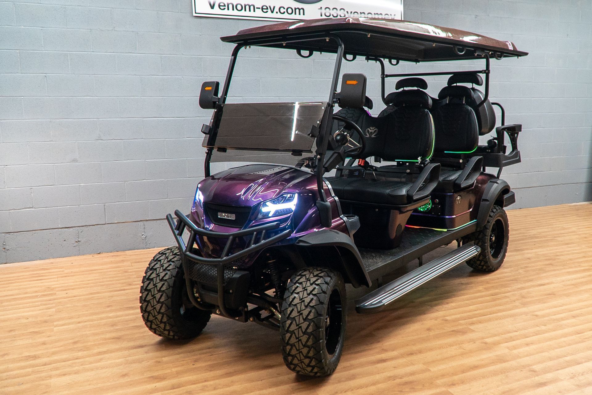 Purple and black off-road utility vehicle with roof and roll cage, parked indoors on a wooden floor.