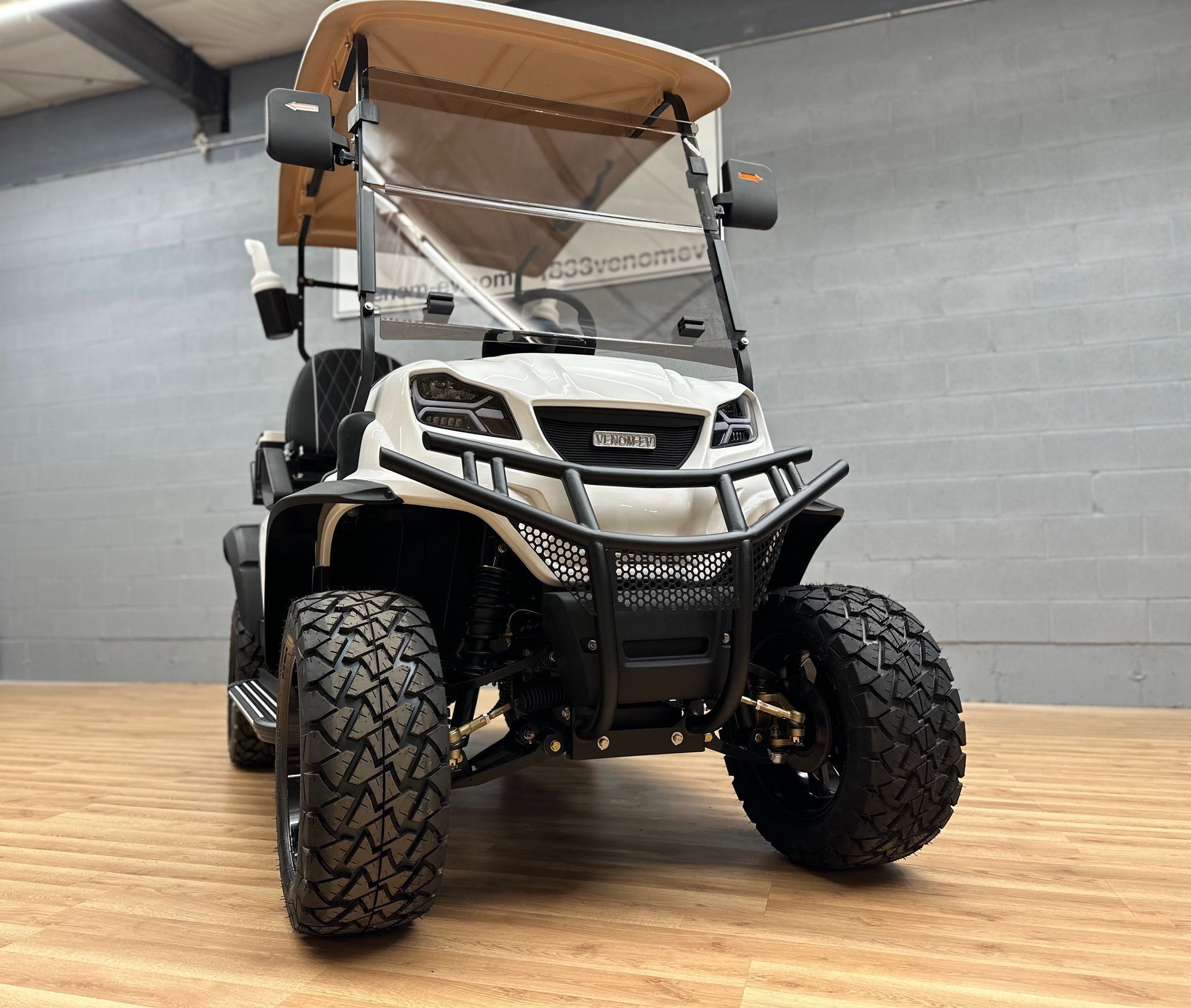 Black and white off-road golf cart with tan roof, parked indoors on a wooden floor.