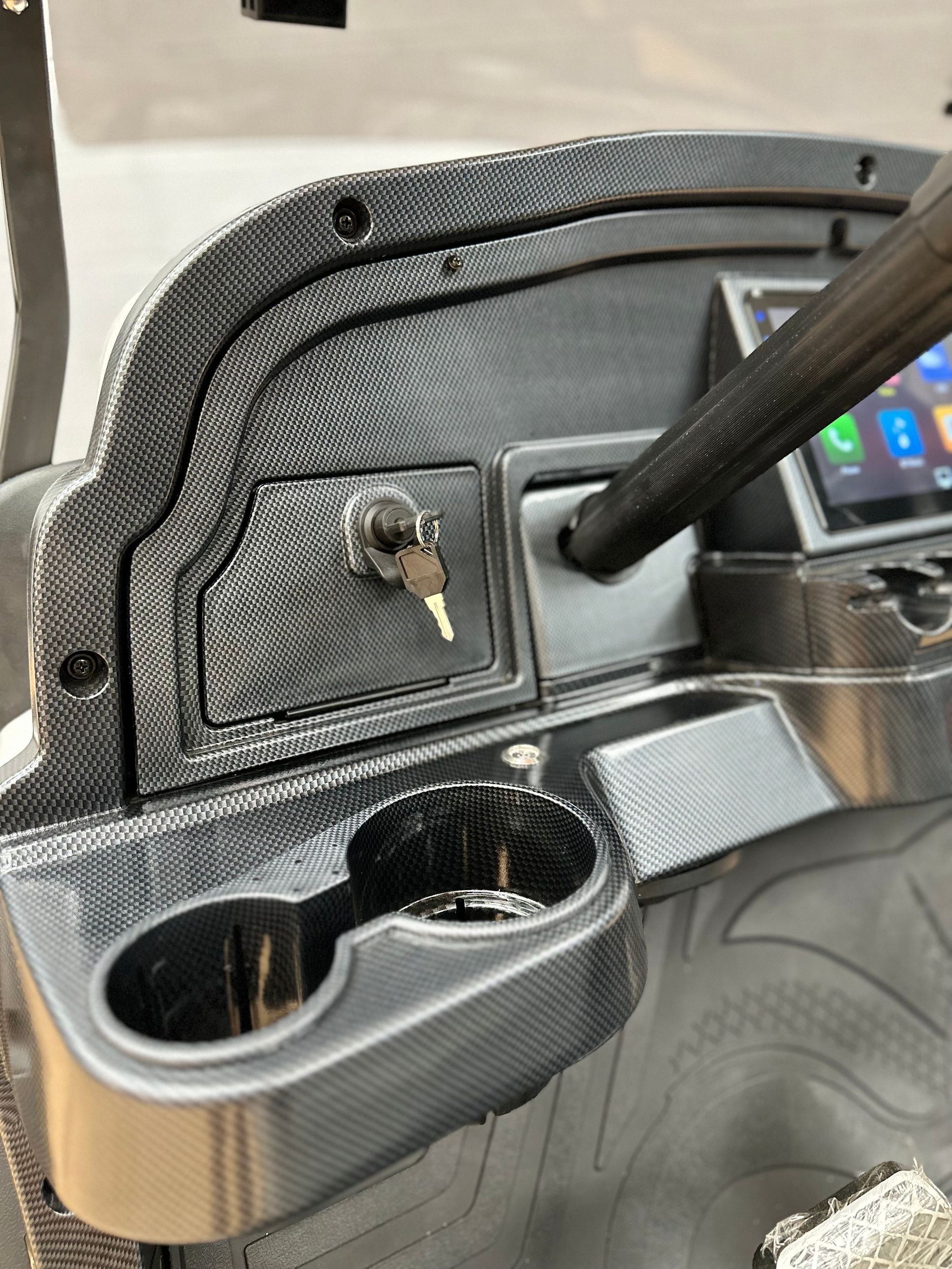 Close-up of a black molded panel with a key in a lock and a cup holder, likely on a vehicle dashboard.