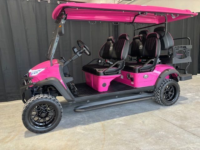 Pink golf cart with black seats and roof parked beside a gray wall.