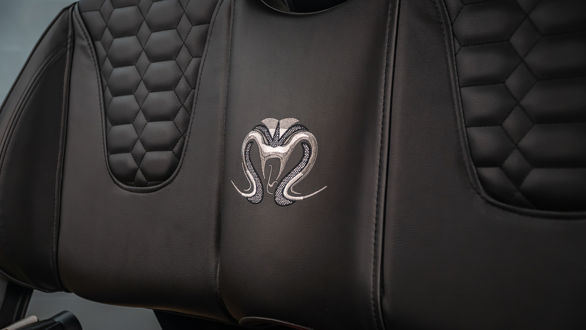 Black leather car seat with quilted panels and a silver Ram logo in the center
