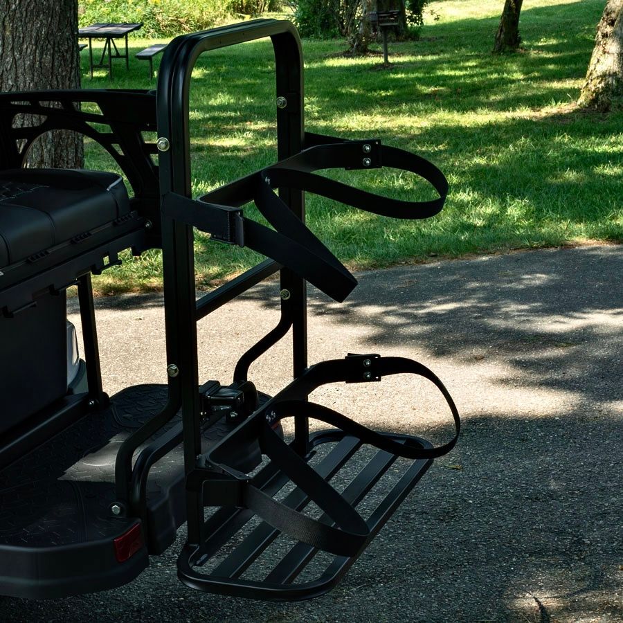 Black metal wheelchair bike attachment with footrests on a paved path in a sunny park