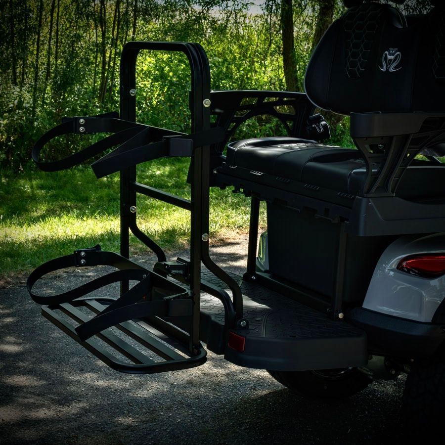 Black mobility lift attached to a golf cart parked on a shaded wooded path.