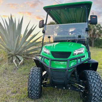 Green all-terrain utility vehicle parked in a field beside a large agave plant.