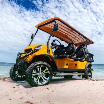 Yellow off-road golf cart on a sandy beach under a striped canopy, with the ocean in the background.