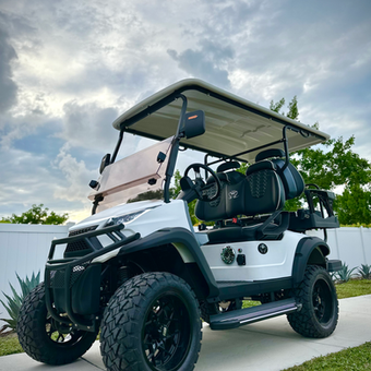 White off-road golf cart with black accents parked on grass under a cloudy sky