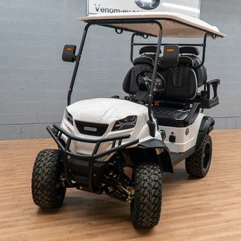 White and black off-road golf cart with canopy, front view, parked indoors on a concrete floor.