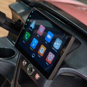 Car dashboard with a touchscreen infotainment display showing colorful app icons and a steering wheel below