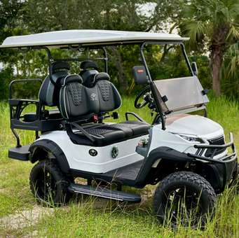 White golf cart on grass with black seats and canopy, parked outdoors among trees