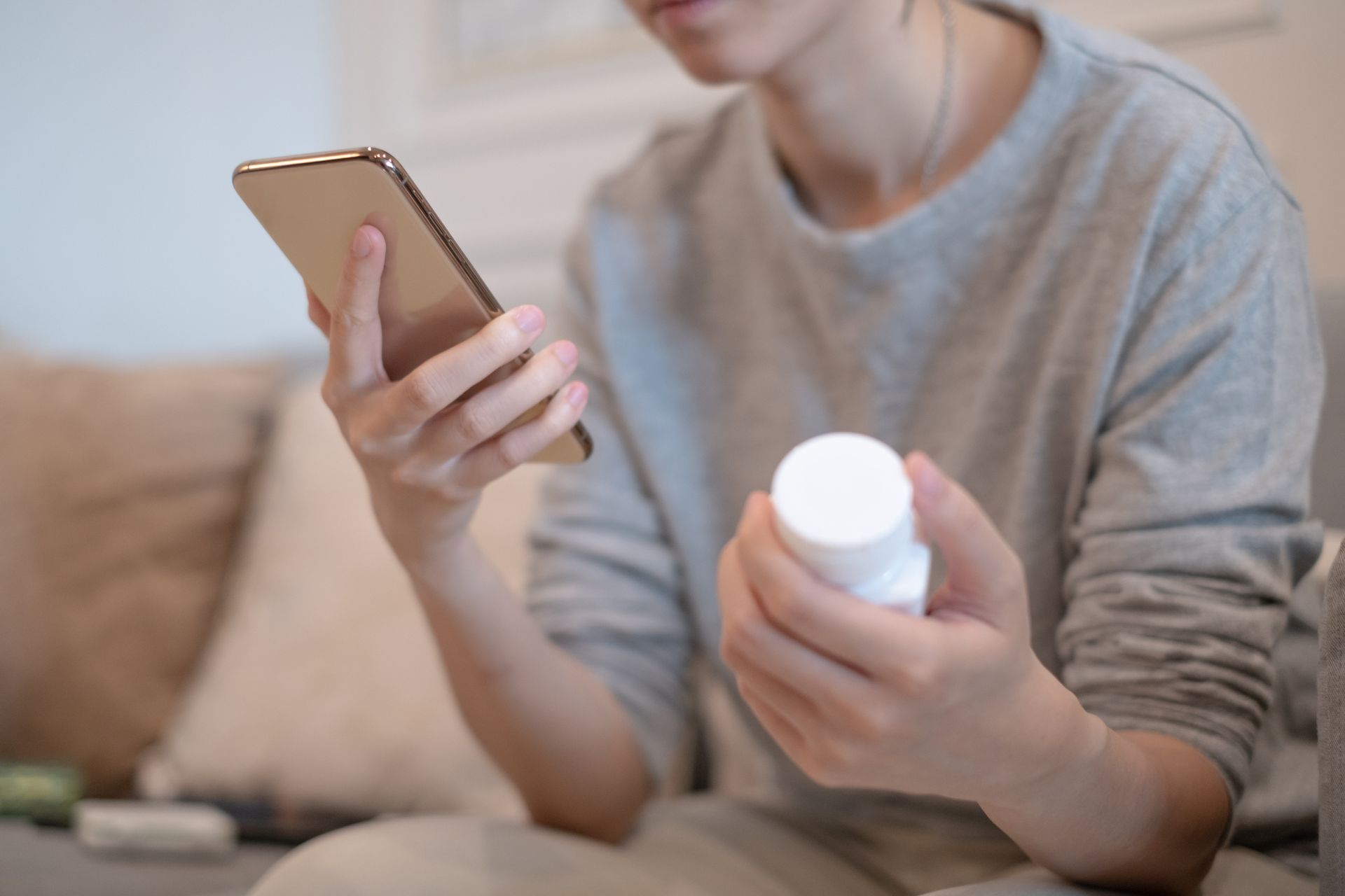 A woman is holding a bottle of pills and a cell phone.