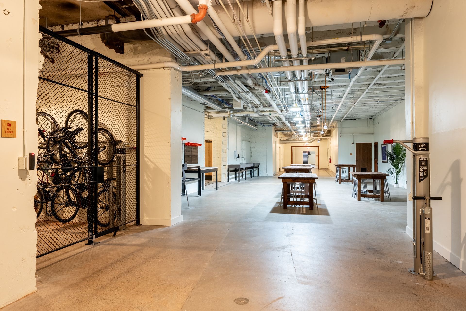 Indoor space with bicycles on a rack, tables, and exposed pipes and ceiling structures.