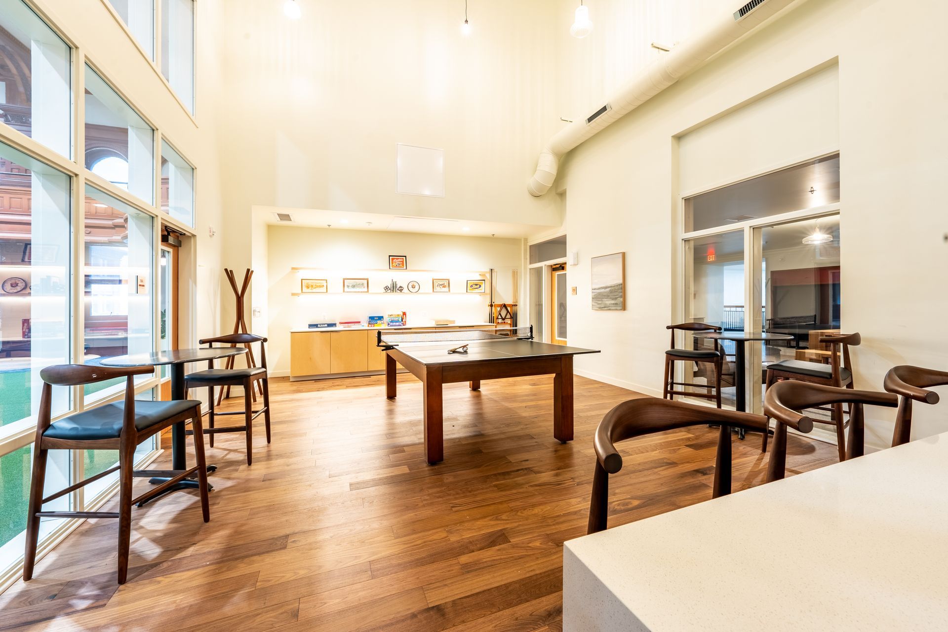 Spacious, well-lit room with wood floors and tall windows. Tables and chairs are arranged around a pool table.