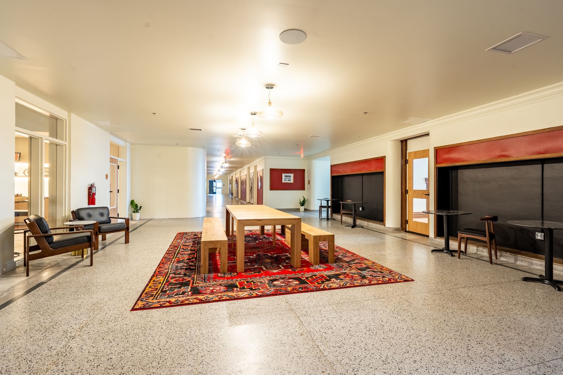 Hallway with seating and a large rug centered under a wooden table and benches.