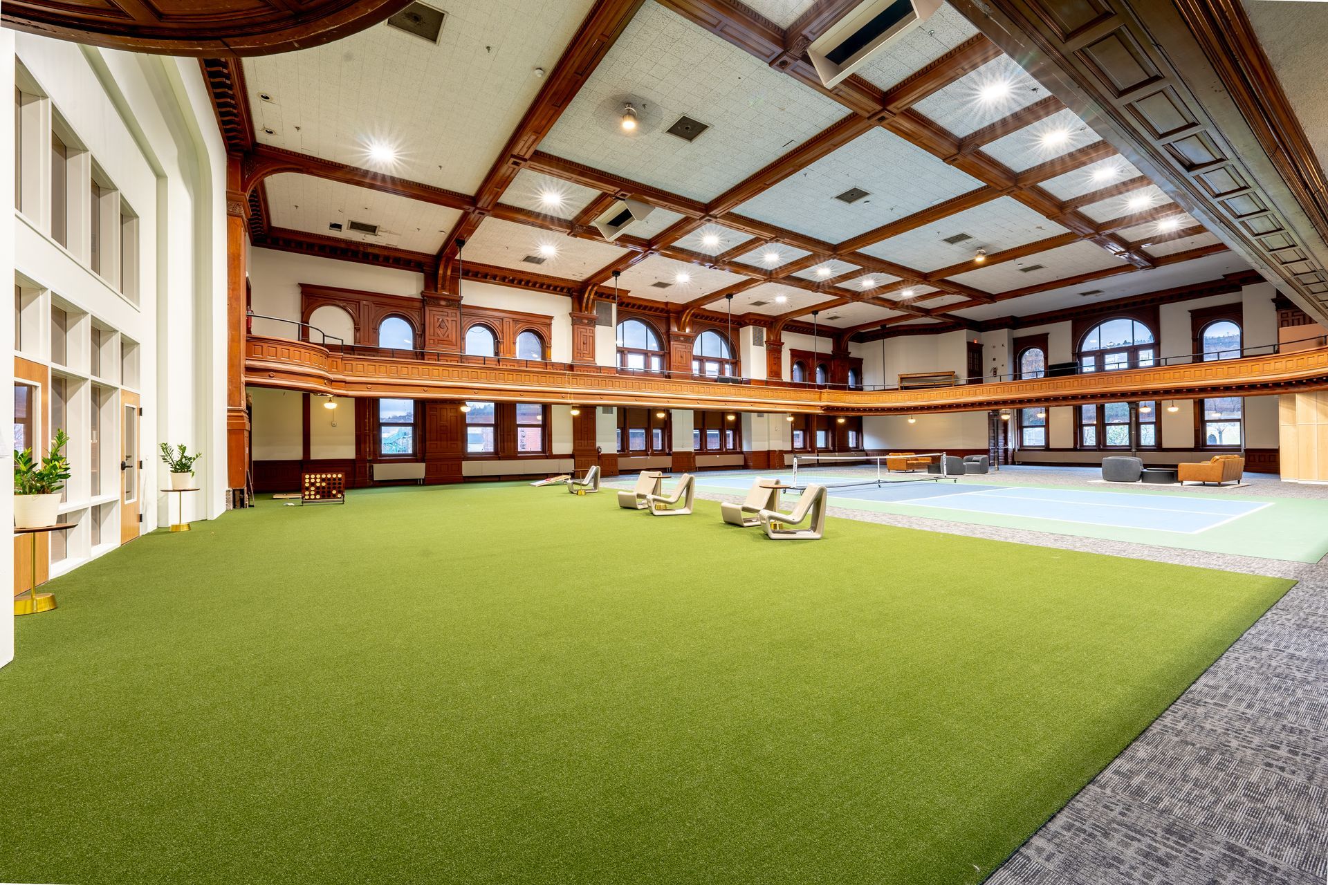 Spacious room with a green turf floor and wooden beams; chairs and balcony.