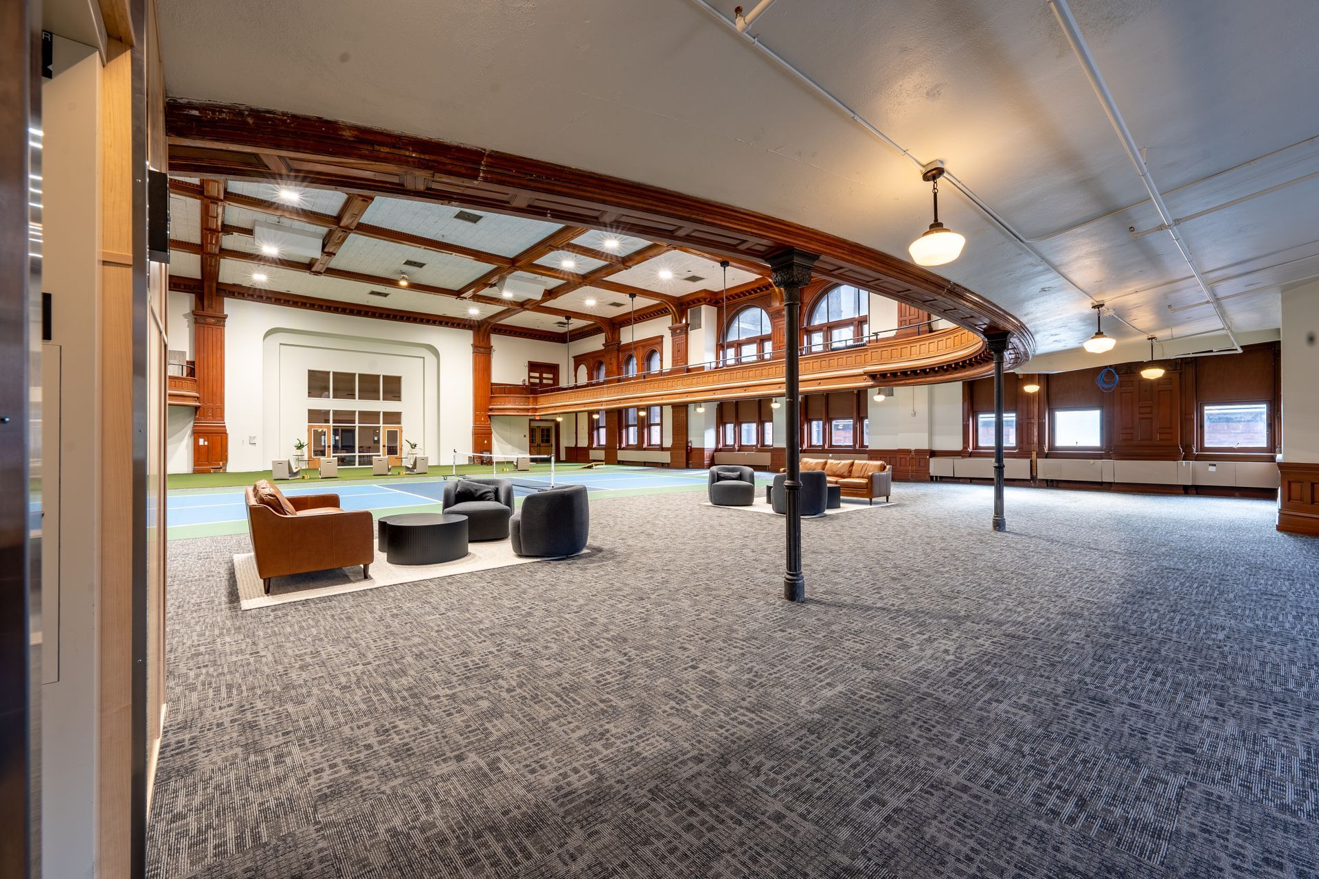 Spacious room with seating, carpeted floor, and wooden beams. White walls with windows and arched ceiling.