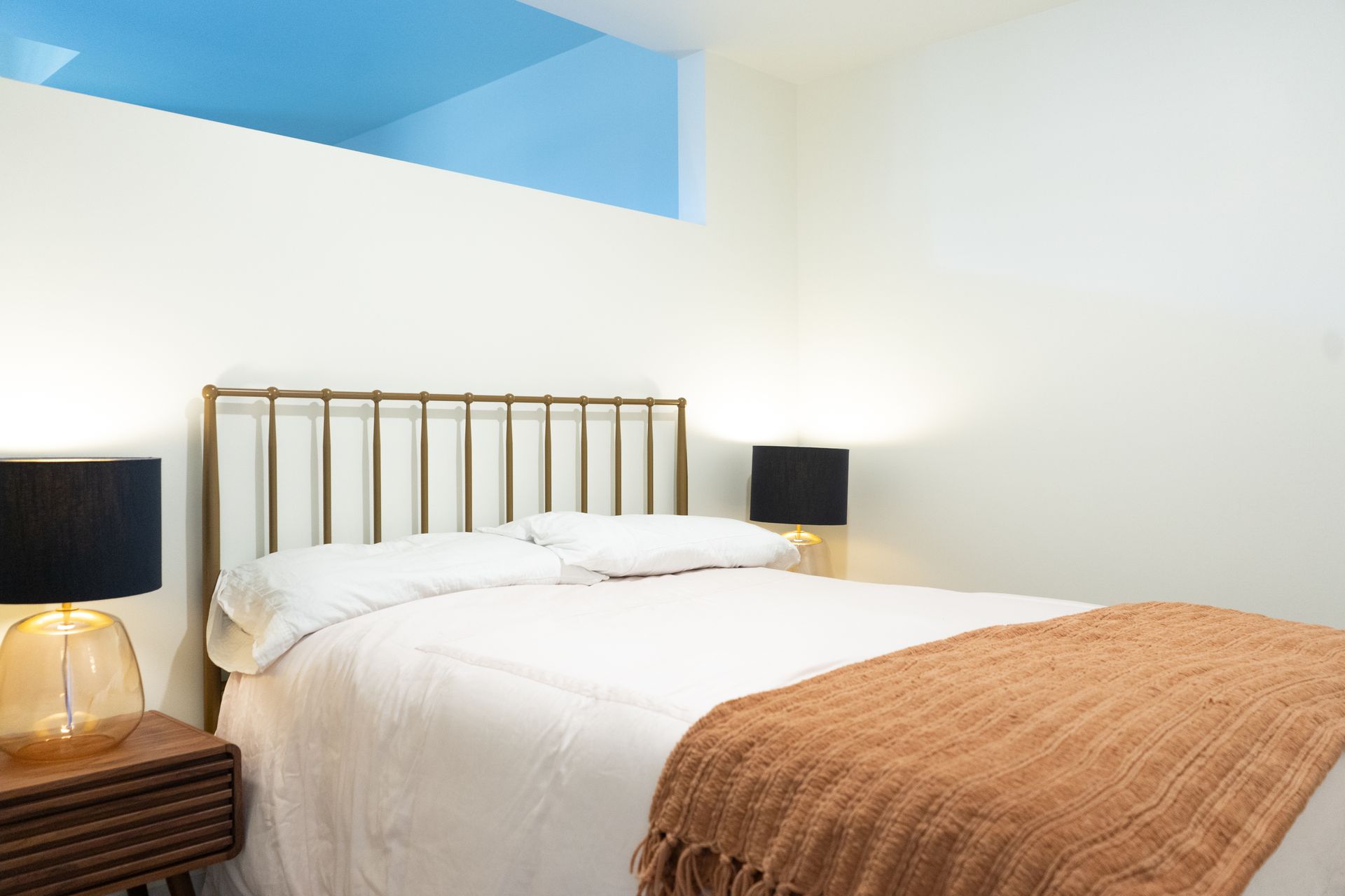 Bedroom with gold bed frame, nightstands, lamps, and a white and orange bedspread.