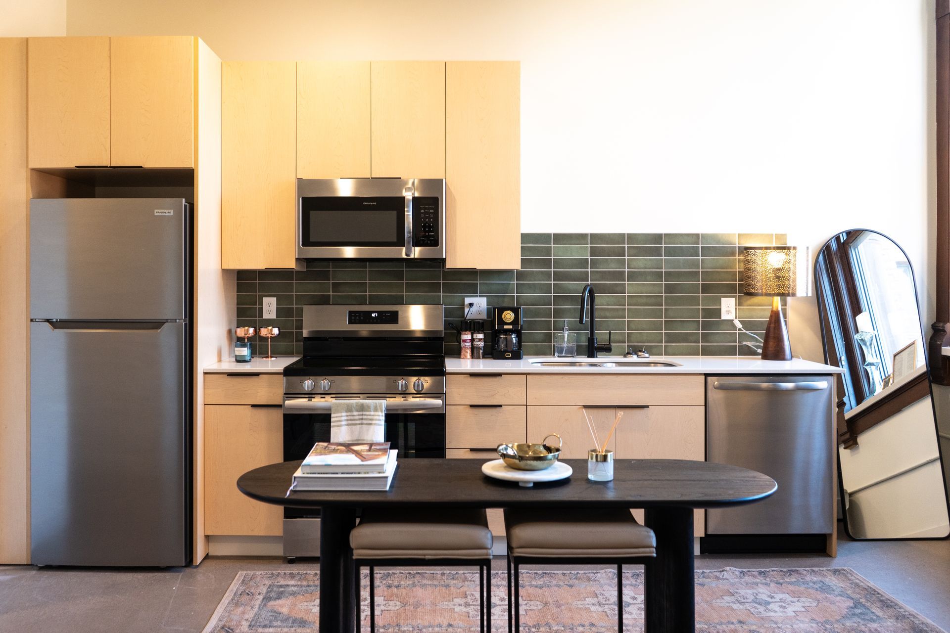 Modern kitchen with wooden cabinets, stainless steel appliances, and a dark oval dining table.