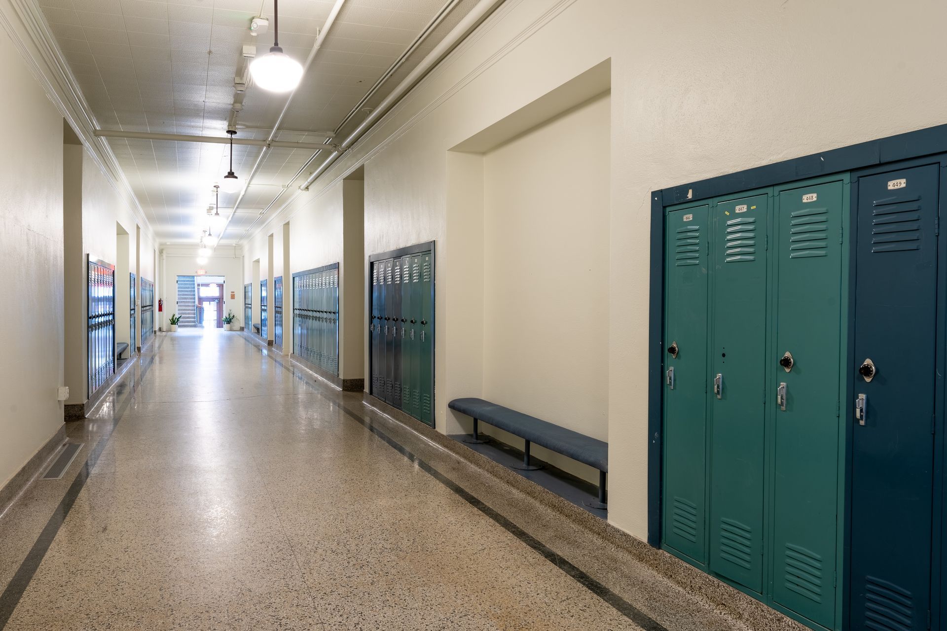 School hallway with lockers, a bench, and overhead lights.