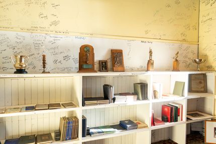Books and trophies on shelves beneath a wall with signatures.