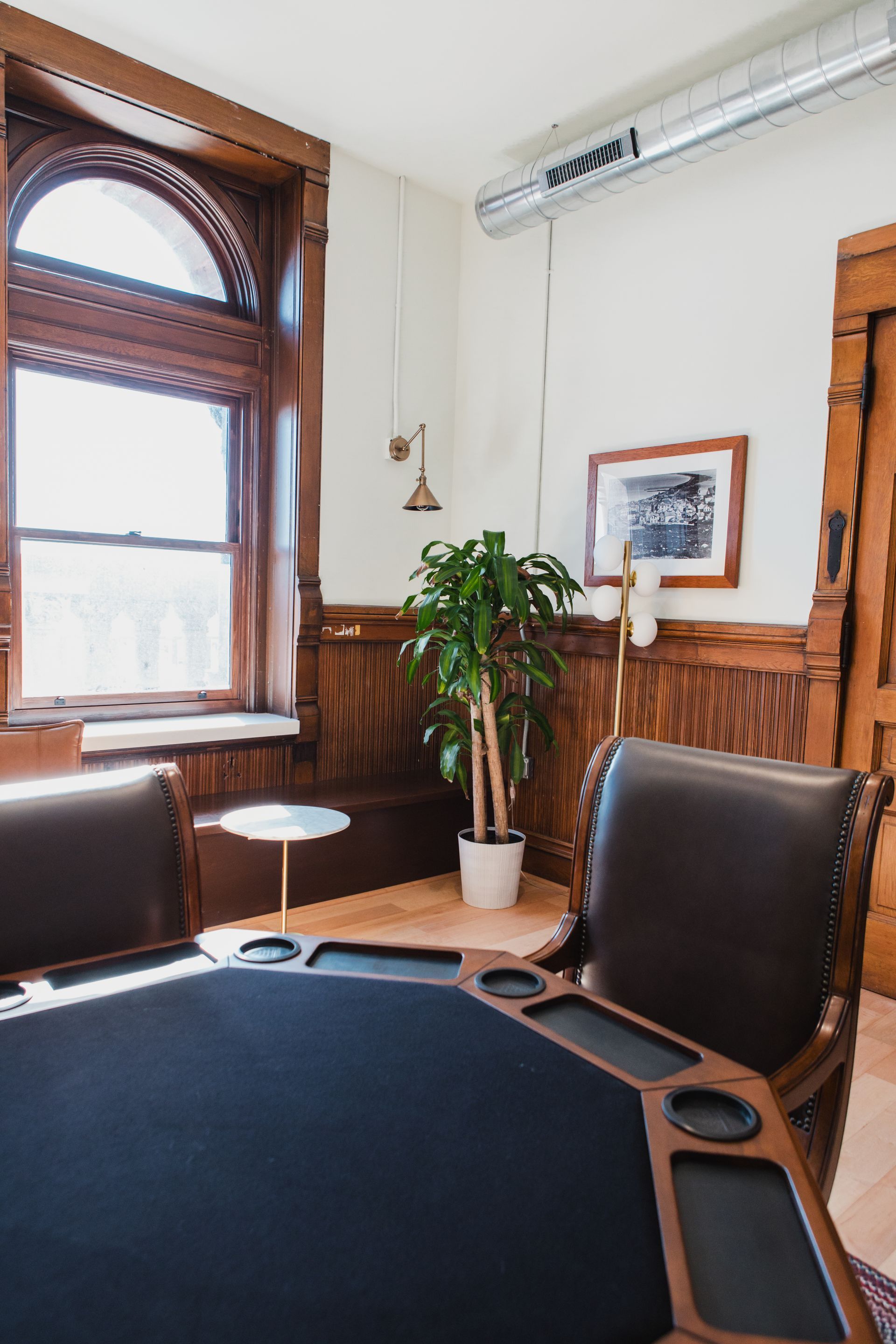 Poker table in a room with wood paneling, a large window, and two leather chairs.
