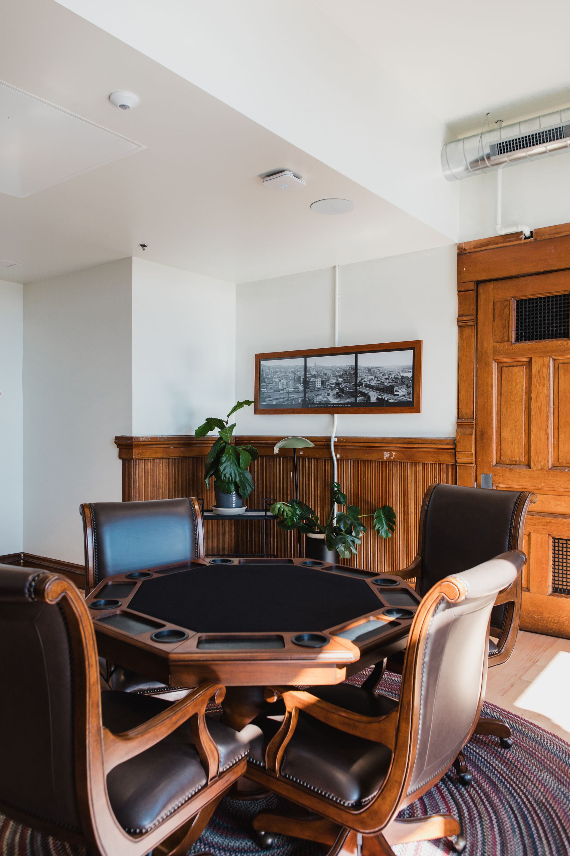 Poker table surrounded by leather chairs in a room with wood paneling and a cityscape photograph.