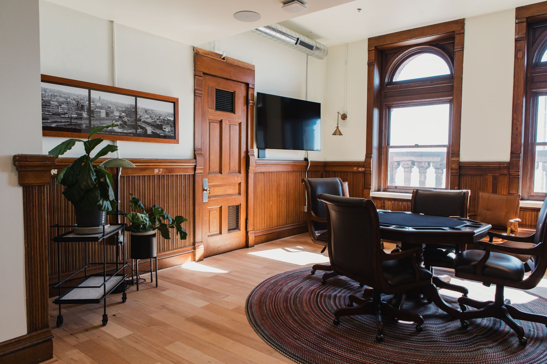 Office with wooden paneling, round table, leather chairs, and large windows.