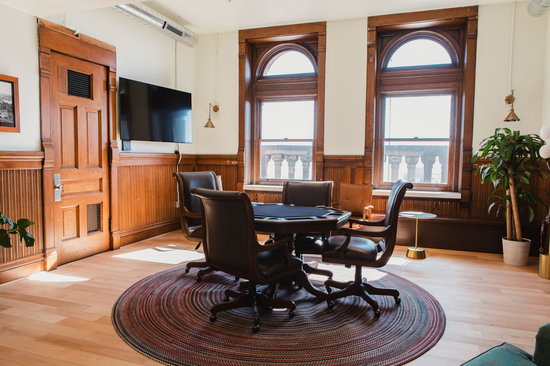 Elegant room with wood paneling, poker table, leather chairs, and arched windows.