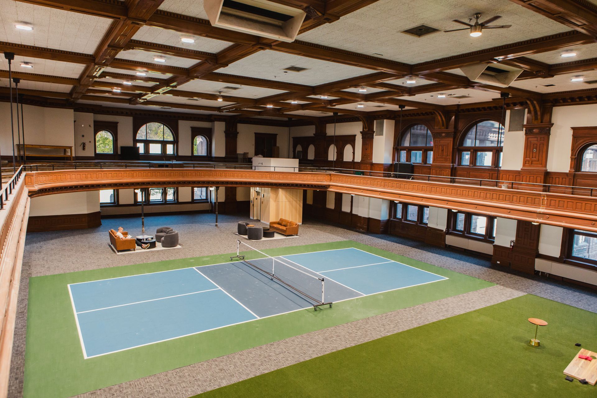 Indoor pickleball court with blue and green court, in a room with a balcony.