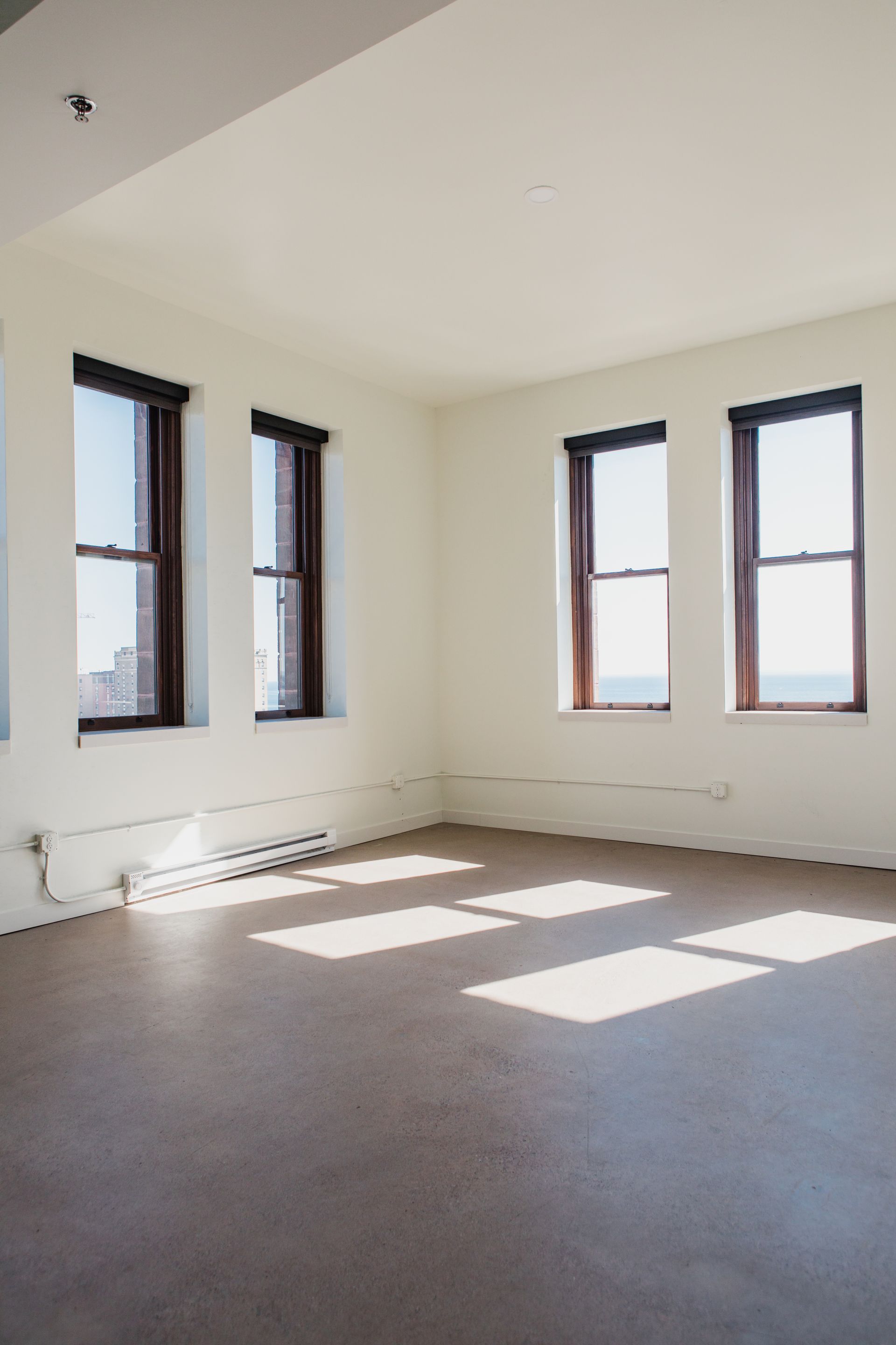 Empty room with large windows, sunlight, and a neutral-toned floor.