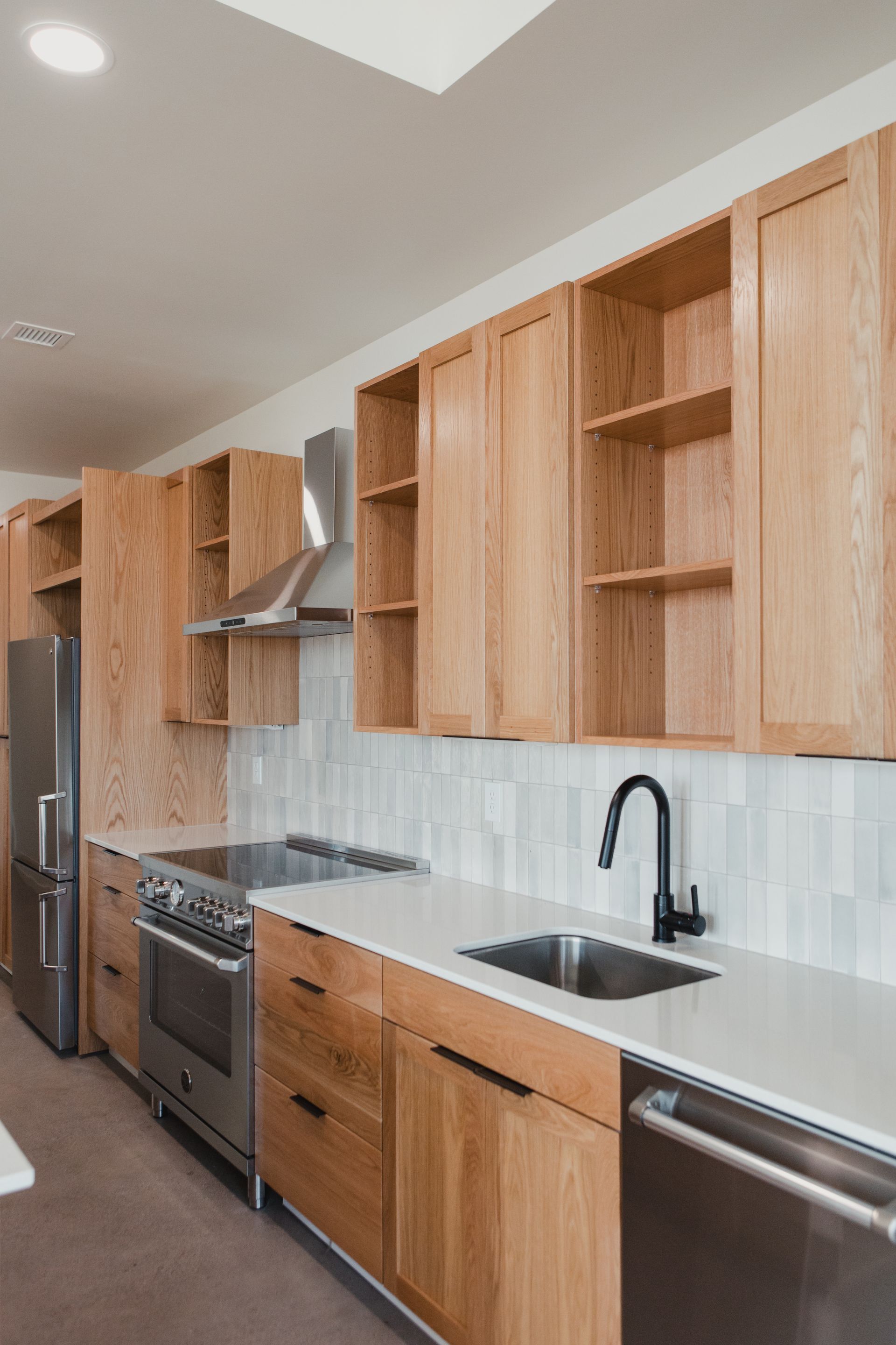 Modern kitchen with light wood cabinets, stainless steel appliances, and white countertops.