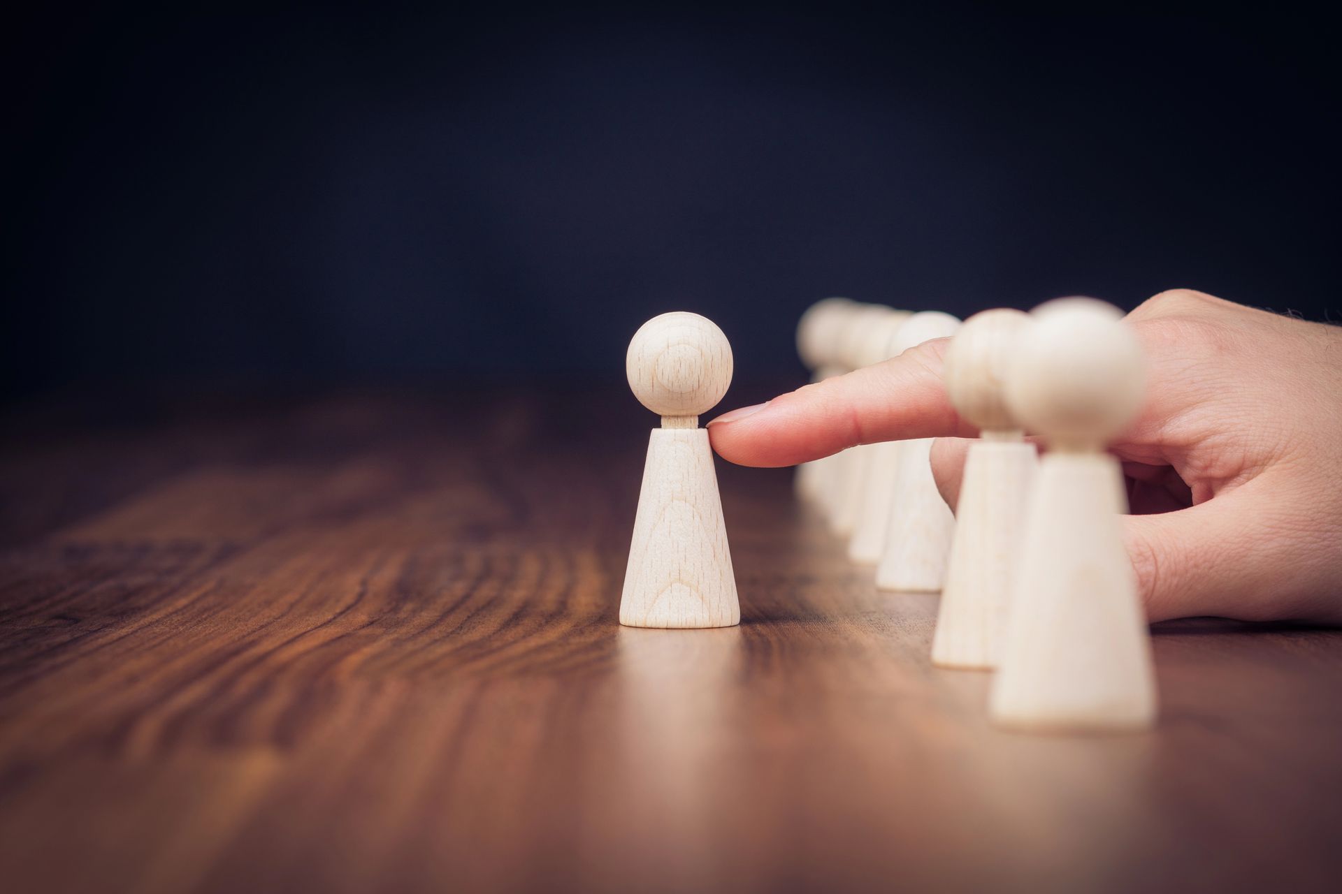 Dedo tocando una pieza de juego de madera, seleccionándola de una línea de piezas similares sobre una superficie de madera.