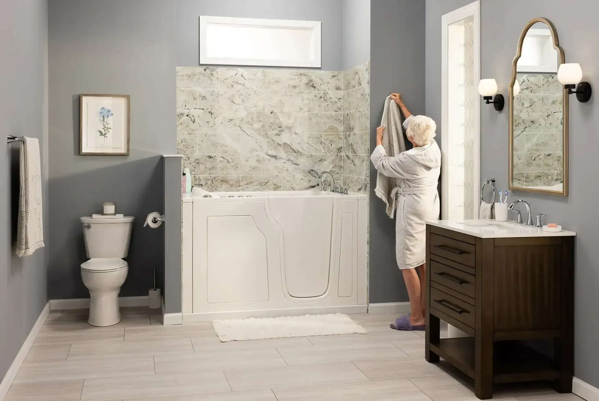 Person painting a bathroom wall beside a toilet, vanity, and tub surround