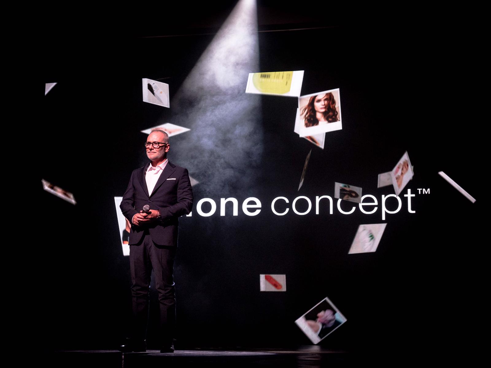 Un hombre con traje está parado frente a una pantalla que dice un concepto.