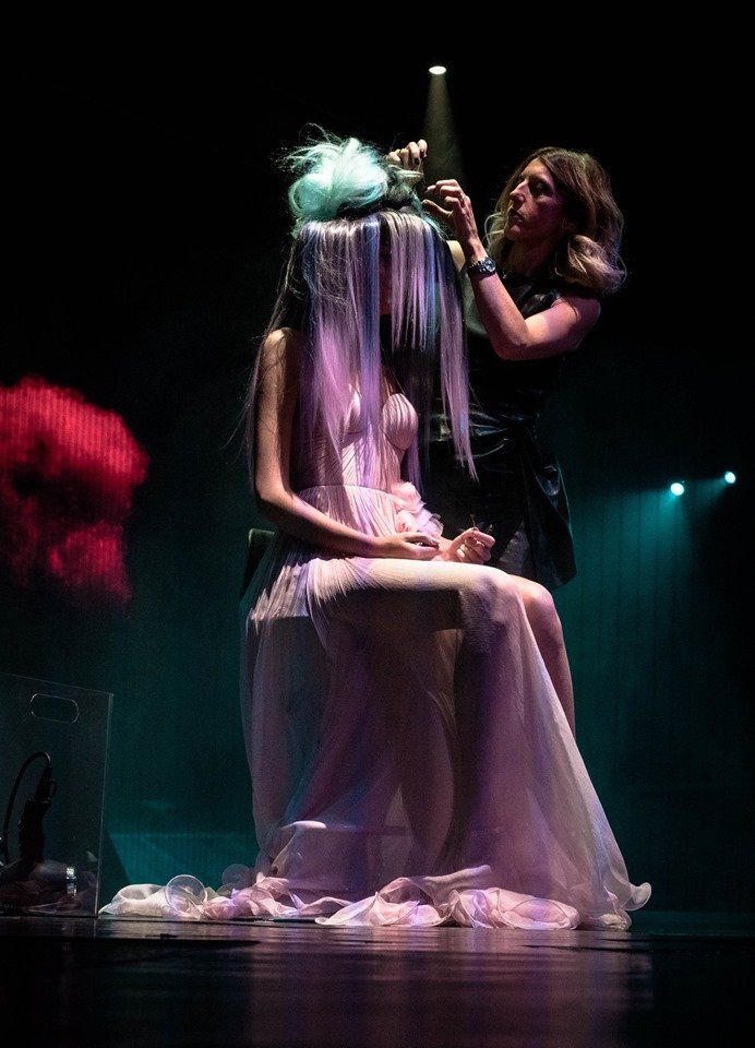 Una mujer está sentada en un escenario mientras un peluquero le peina el cabello.