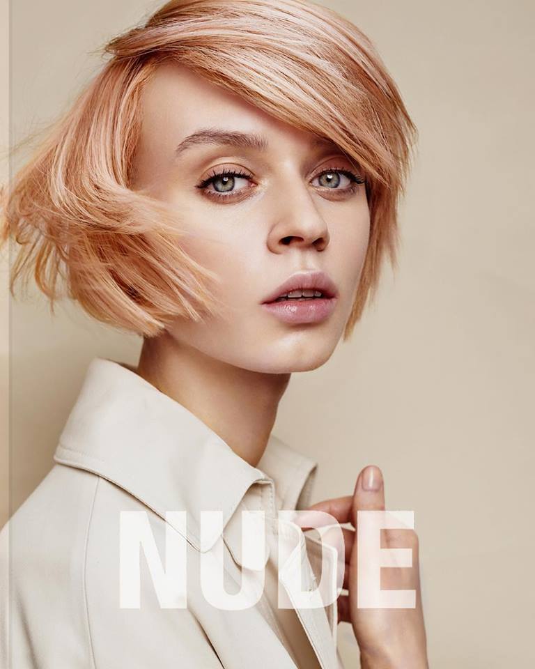 Una mujer con cabello corto de color rosa lleva una bata blanca.