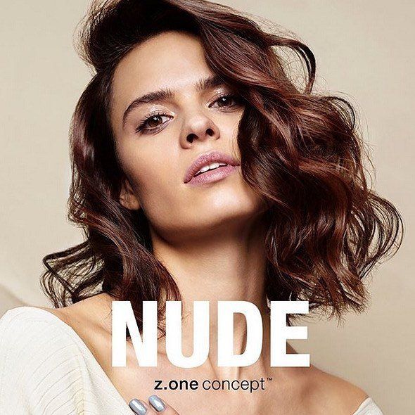 Una mujer de cabello castaño lleva una camisa blanca con las palabras 