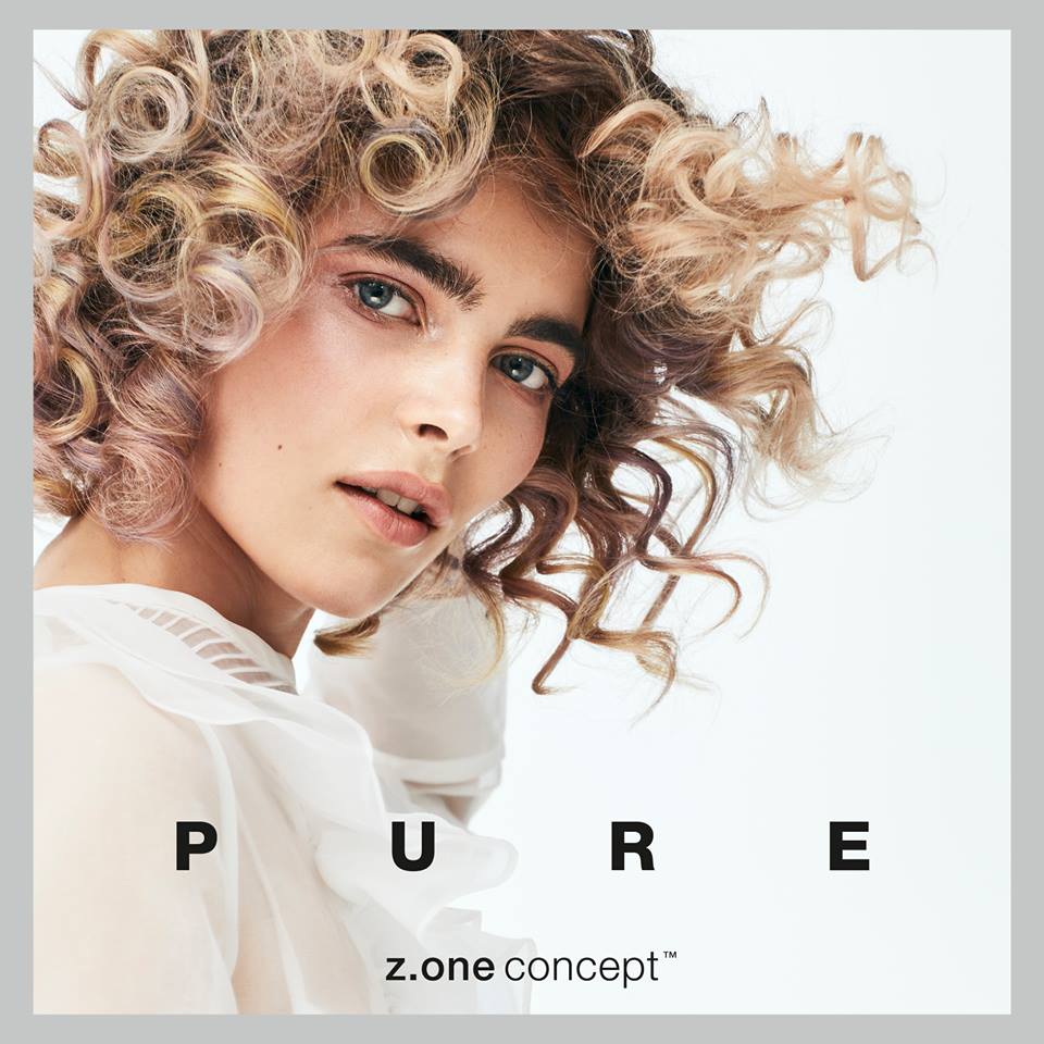 Una mujer con cabello rizado lleva una camisa blanca.